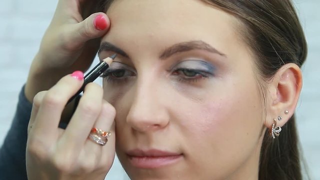 Professional make-up artist applying mascara on eyelashes of model in white room. Beauty, make up and fashion concept