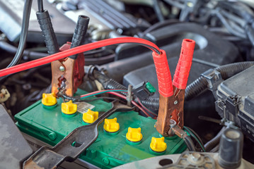 car battery clamped with black and red jumper cable to recharge the power