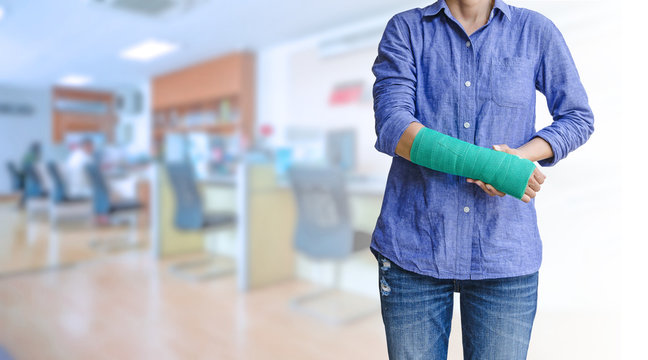 worker woman accident on arm with green arm cast on blurred business office working space background