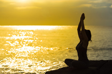 Fototapeta premium Young woman silhouette meditating and practicing yoga on the beach at sunset.Slim girl with yoga.