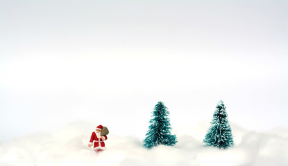 Miniature figure of Santa Claus and artificial Christmas trees with snow background using for Christmas decoration concept.