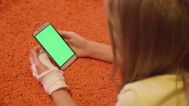 Young caucasian blonde with broken left hand look at green screen of the smartphone. Close up view