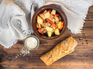 Baked meat with potatoes, bread, salt and spices on the background of wooden table and coarse cloth. Roast potatoes in a clay bowl with a wooden spoon. Rural still life. The top view.