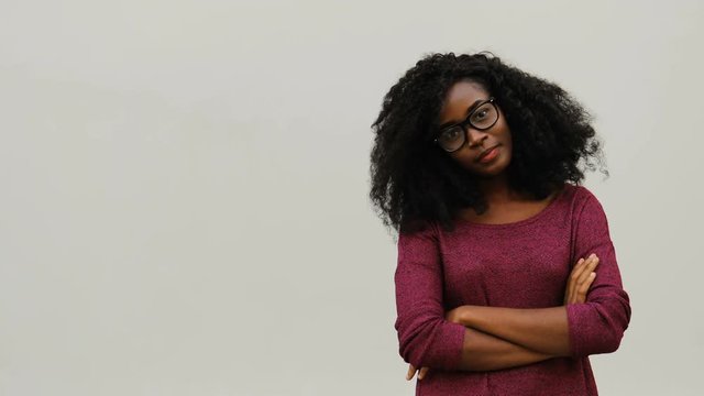 Portrait of pretty African girl in glasses with curly hair wearing pink sweater. Young woman standing on white background.