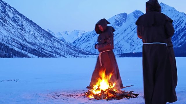 Group of monks in brown cloaks of the order of St. Francis are circling around the fire