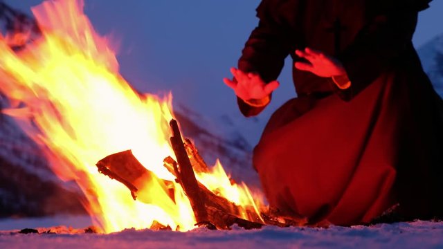 Group of monks in brown cloaks of the order of St. Francis are warming hands by the fire