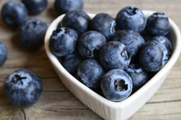 Freshly picked blueberries in a white heart shaped bowl on old wooden background close up.Fresh organic blueberry.
Bilberries.Healthy eating,vegan diet or raw food concept.Selective focus.