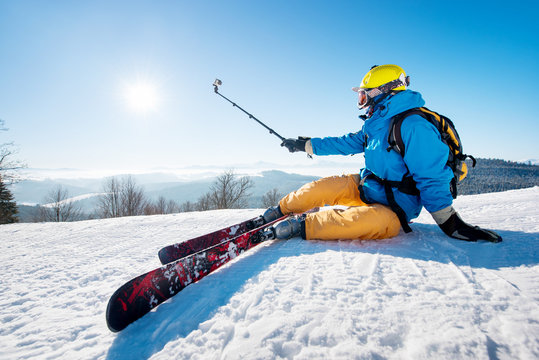 Shot of a skier sitting on the ski slope taking a selfie using selfie stick resting relaxing extreme recreation active lifestyle activity technology smart phone mobility internet online concept