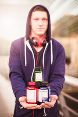 The young sporty man standing outdoor and holding boxes with protein pills in hands