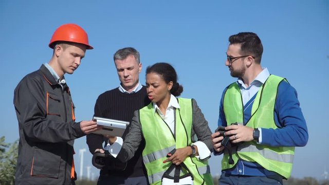 Four different people standing and putting on virtual reality headsets with windmills in the background