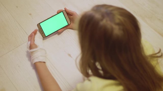 Young caucasian blonde with broken left hand look at green screen of the smartphone. Close up view