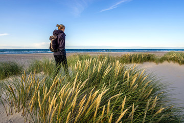 Young woman hiking in coastal dune grass at beach of North Sea.