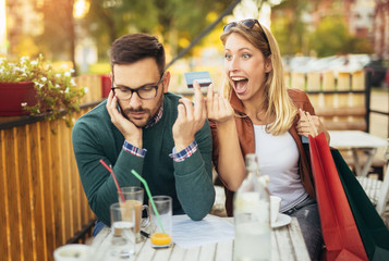 Woman sitting in cafe with handsome man and colorful shopping bags, cup of coffee, holding credit card. Online shopping concept. Beautiful couple smiling.