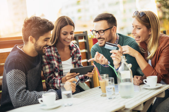 Friends having a coffee together. Two women and two men at cafe shopping on line with digital tablet