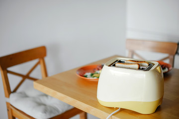 yellow toaster with toasted bread inside on the table in the kitchen interior. - obrazy, fototapety, plakaty