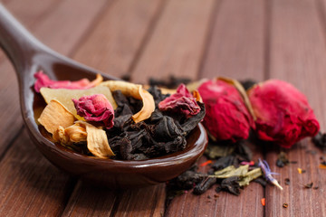Composition of natural tea with a rose. Macro photo of tea petals on a ceramic spoon with a  rose. Tea with the ingredients of flowers and rose tea located on a wooden Board.