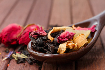 Composition of natural tea with a rose. Macro photo of tea petals on a ceramic spoon with a  rose. Tea with the ingredients of flowers and rose tea located on a wooden Board.