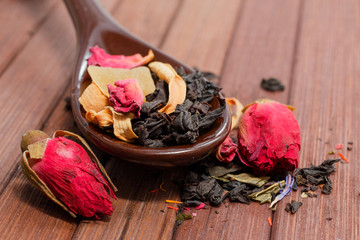 Composition of natural tea with a rose. Macro photo of tea petals on a ceramic spoon with a  rose....