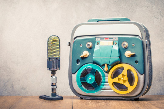 Retro reel to reel tape recorder circa 60s and ribbon studio microphone on wooden table front concrete wall background. Vintage style filtered photo