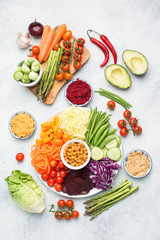 Healthy eating concept, top view of rainbow buddha bowl, various vegetables, carrot, courgette, cabbage, chickpeas, cucumber and tomatoes, on wooden board on white table, top view, selective focus