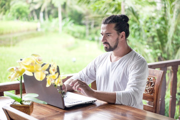 Freelance work on laptop. Man sitting at wooden desk inside garden working on computer