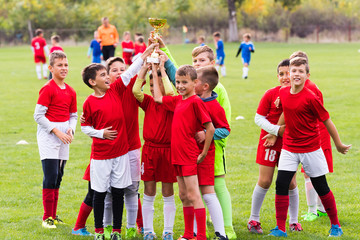 Kids soccer football -  children players celebrating with a trophy after match on soccer field