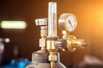 Close-up of a metal gas cylinder with a reducer and a pressure sensor in the background industrial workshop