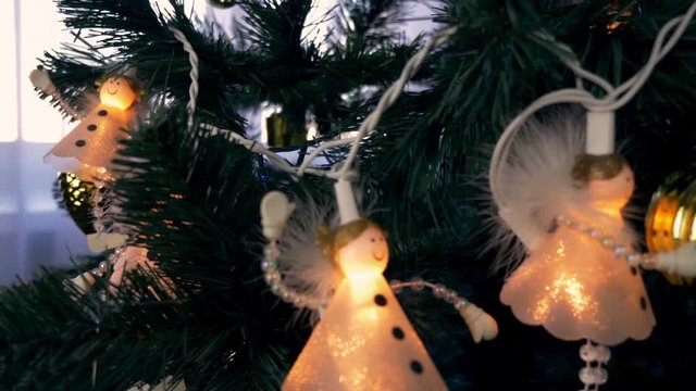 Christmas lights on fir tree. Green firtree with white lights of Angels. Angels hange on christmas tree branches. Close up dolly shot.