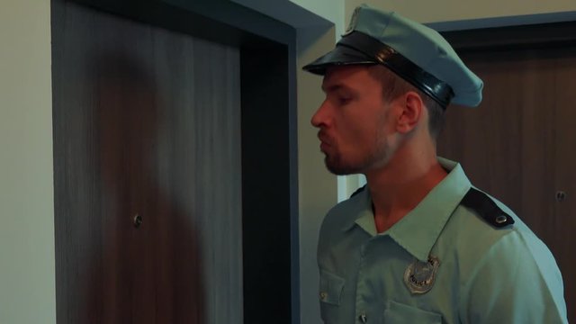 A young police officer knocks on an apartment door