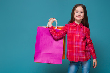 Cute little girl in checkered shirt with brunet hair hold different bags