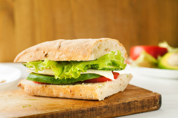 Vegetarian sandwich with avocado, tomato, egg and green salad on a wooden board
