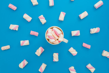 Cappuccino mug with marshmallows on blue background. Flat lay, top view