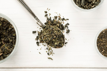 Dry tea in a metal spoon on a white wooden table, top view