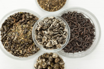 Different dry tea in a small glass dishes on a white wooden table
