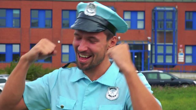 A young police officer celebrates - closeup - a police station in the background