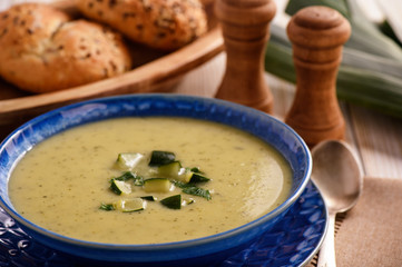 Cream soup with leek and zucchini on white wooden background.