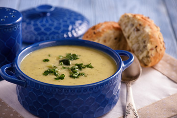 Cream soup with leek and zucchini on white wooden background.