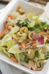 Fresh vegetables and bacon salad in a white bowl. A healthy iceberg salad with olives served on a wooden rustic table.