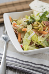 Fresh vegetables and bacon salad in a white bowl. A healthy iceberg salad with olives served on a wooden rustic table.