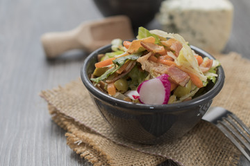 Fresh vegetables and bacon salad in a black bowl. A healthy iceberg salad with olives served on a wooden rustic table.
