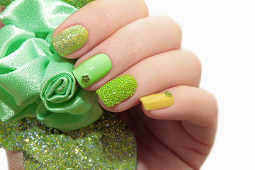 Pastel green manicure with sequins and rhinestones on a white background closeup.