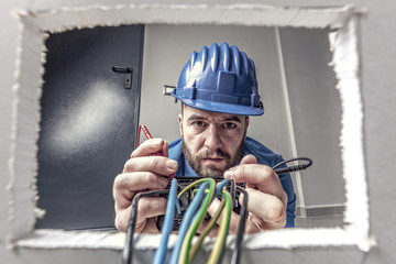  wide angle image, view from inside a wall socket of an electrician who connects cables to an...
