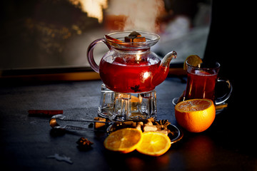 The atmosphere of new year atmosphere. Kettle on stand with warming candles. In a kettle of mulled wine or hibiscus tea with lemon. Cinnamon sticks and orange.