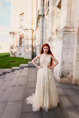 Obraz premium Beautiful red-haired girl with long curly hair in the bride, in a long lace dress. A natural beauty.