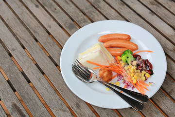 Breakfast with sandwich, sausage and salad in a white dish.