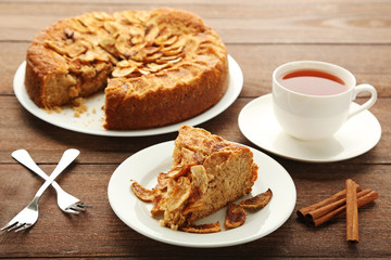 Slice of apple cake in plate with cup of tea on brown wooden table
