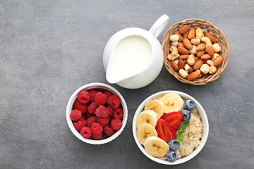 Oatmeal in bowl with berries, nuts and jar of milk on wooden table
