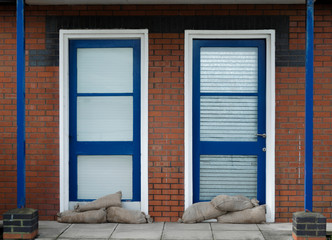 Sandbags stacked against glass and wood doors with roller shutters behind the doors
