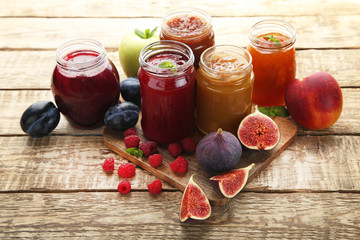 Glass jars with different kinds of jam and berries on wooden table