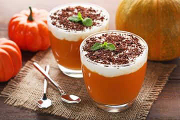 Pumpkin smoothie in glasses with spoons on wooden table